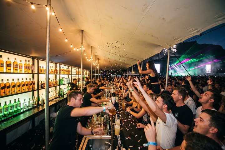 Guests three deep at the bar while the bartenders pour, confetti in the air and the main stage lit behind